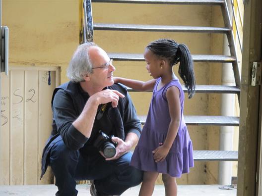 Dieses Bild zeigt Frédéric Druot wie er sich kniend mit einem kleinen Mädchen auf Augenhöhe unterhält.