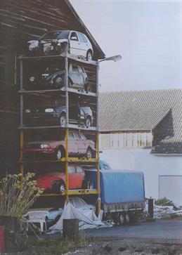 Photograph by the artist Markus Ambach, A stack of car bodies in a shelving system in the courtyard behind a house can be seen.